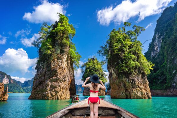 Beautiful girl standing on the boat and looking to mountains in Ratchaprapha Dam at Khao Sok National Park, Surat Thani Province, Thailand.
